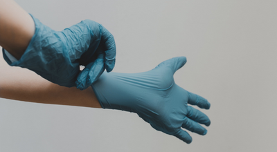 Imagen muestra las manos de profesinal de la salud colocándose guantes quirúrgicos