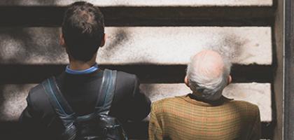 Un hombre joven sube una escalera junto a un adulto mayor, dando la espalda a la cámara